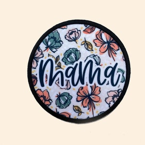 May include: A round, white fabric patch with a black border and a floral pattern. The word "mama" is written in black cursive lettering.