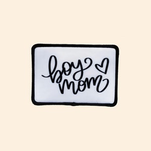 May include: White iron-on patch with black embroidered text that reads "boy mom" with a small heart symbol.