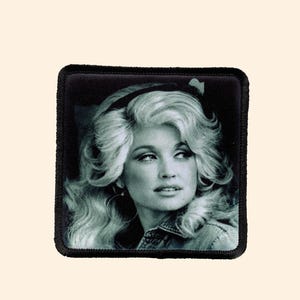May include: Black and white photo of a woman with blonde hair and a black headband. The photo is on a black fabric patch.
