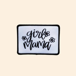 May include: White iron-on patch with black embroidered text that reads "girl mama" with two small flower designs on either side of the text.