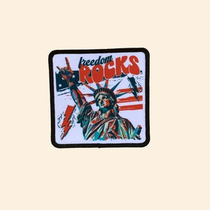 May include: A white patch with a black border featuring a stylized image of the Statue of Liberty with a peace sign and the text "freedom rocks" in red and orange letters.