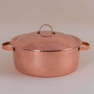Puede incluir: Una olla redonda de cobre martillado con su tapa a juego. La olla cuenta con dos asas laterales y un pequeño mango arqueado en el centro de la tapa. La superficie exterior presenta un acabado texturizado con hoyuelos en todo el cuerpo.