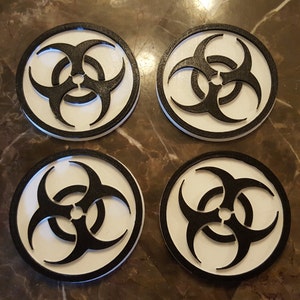 May include: Four white coasters with a black biohazard symbol printed on each. The coasters are round and have a raised edge.