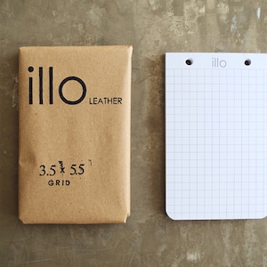 May include: A brown paper package with the text "illo LEATHER 3.5 x 5.5 GRID" printed on it. Next to the package is a white grid notebook with the text "illo" printed on the top.
