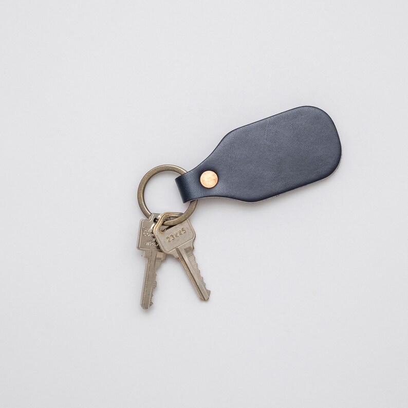 Indigo leather key tag holding two silver keys on a light grey background