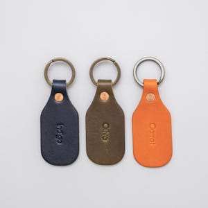 Three leather key tags, blue, green, and orange, on a light grey background