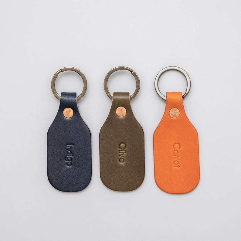 Three leather key tags, blue, green, and orange, on a light grey background