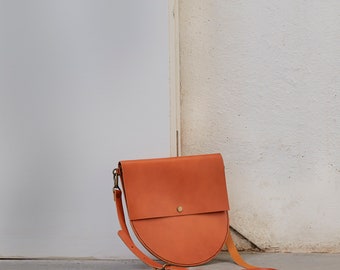 May include: A brown leather crossbody bag with a flap closure and a rounded bottom. The bag has a brass buckle and a strap.