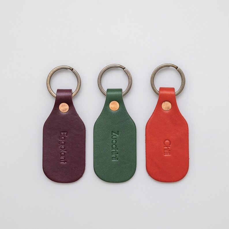 Three leather key tags, purple, green, and red on a light grey background