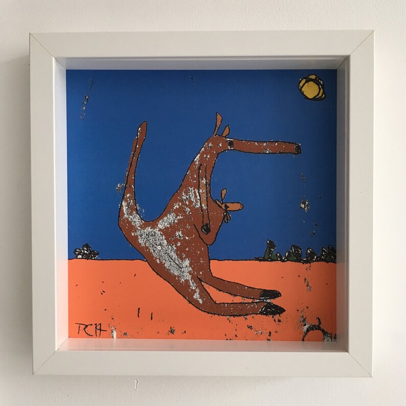 May include: A framed illustration of a brown kangaroo with a joey in its pouch, standing on a peach-colored ground against a blue sky with a yellow sun. The artwork is signed "TCH" in the bottom left corner.