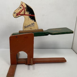 May include: Vintage wooden rocking horse toy painted in white, red, and black with the words "Bounce-a-babe" on the horse's head. The horse is attached to a wooden base painted in green and orange.