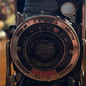 Peut inclure: Appareil photo Plenax noir et argent vintage avec un objectif Tripar. L'appareil photo dispose d'un cadran pour la vitesse d'obturation et les ouvertures du diaphragme. Il est marqué "Made in America by Agfa Ansco Corporation Binghamton, NY."