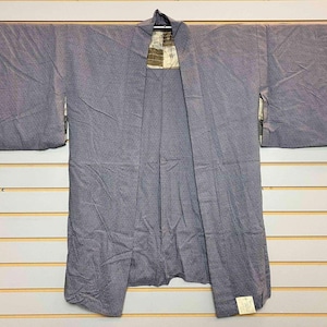 May include: A light purple haori jacket featuring a subtle, fine geometric pattern across the fabric. The garment has wide, rectangular sleeves, an open front design, and a visible cream-coloured lining with a dark grid pattern at the neck.