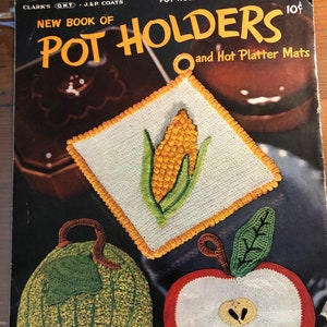 Puede incluir: Una portada de libro vintage que presenta un patrón para posavasos de ganchillo. La portada muestra tres posavasos: una manzana verde, una manzana roja y una mazorca de maíz. El título del libro es "New Book of Pot Holders" y el subtítulo es "and Hot Platter Mats".