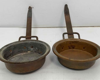 May include: Two antique copper cooking pots with long iron handles. The pots have a worn, aged look and are slightly dented.