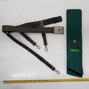 May include: A black and green striped belt with a silver buckle that says "Seattle Consistory No. 2". The belt is attached to two black straps with silver hooks. A green sash with the text "The Henderson Military and Literary Association" is also included.