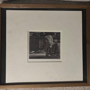 Peut inclure: Photographie encadrée en noir et blanc d'un homme en costume assis à une table. La photo est centrée dans un passe-partout blanc, avec un cadre noir et un cadre en bois.