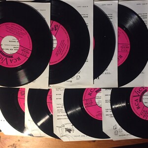 Könnte beinhalten: Eine Sammlung von Vintage-Schallplatten mit rosa Etiketten, die das RCA Victor-Logo tragen. Die Schallplatten sind schwarz und haben eine glänzende Oberfläche. Die Etiketten tragen den Text "RCA Victor" und "45 RPM".