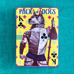 May include: A playing card from a deck called "Pack of Dogs". The card is the King of Clubs and features a dog dressed as a knight with a sword. The card has a yellow, pink, and green background with a diamond pattern.