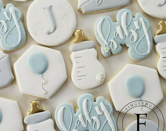 May include: A set of blue and white decorated sugar cookies with various designs including a baby bottle, a balloon, and the word "baby".