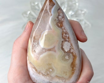 May include: A white, brown, and yellow agate freeform point with a smooth, polished surface. The point is shaped like a teardrop and has a variety of patterns and textures.