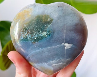 May include: A heart-shaped polished stone with a blue, green, and white color pattern. The stone has a smooth, polished surface.