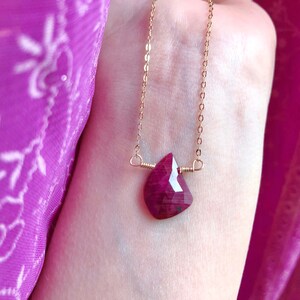 May include: A gold chain necklace with a deep red gemstone pendant. The pendant is a faceted, teardrop-shaped stone.
