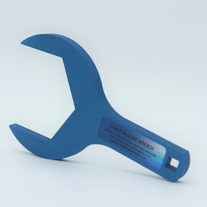 May include: A blue wrench with a square opening at the end of the handle. The wrench is labeled "Shaft Packing Wrench".