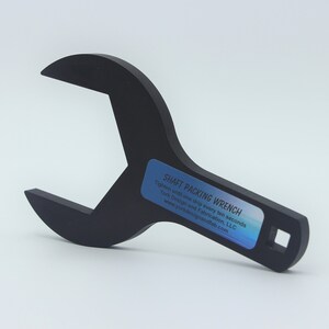 May include: A black metal wrench with a square opening on one end and a hexagonal opening on the other. The wrench is labeled "SHAFT PACKING WRENCH" with instructions to tighten and drop every two seconds. The wrench is designed and fabricated by Work Design and Fabrication, LLC.