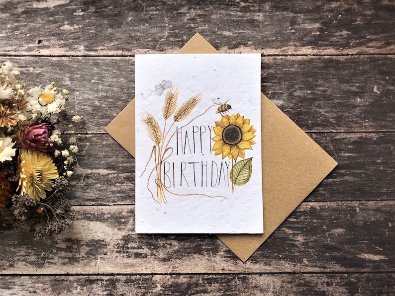 May include: A white card with a sunflower, wheat stalks, a bee, and a butterfly. The card says "Happy Birthday".