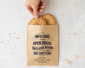May include: A brown paper bag with the text "Welcome to the Open House, Take a look around and Ask Questions" and the contact information "Erika Smith, The Real Estate Company, 555.555.5555". Two cookies are in the bag.