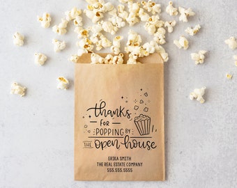 May include: A brown paper bag filled with popcorn with a thank you message that reads "Thanks for popping by the open house". The bag also includes the name Erika Smith, The Real Estate Company, and a phone number.