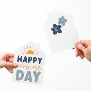 May include: Two white house-shaped cards. One card has a yellow sun and the text "HAPPY closing DAY". The other card has two blue flowers.