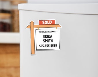 May include: A red and white "SOLD" sign with a wooden frame and a white sign below that reads "THE REAL ESTATE COMPANY" with the name "ERIKA SMITH" and the phone number "555.555.5555" below.