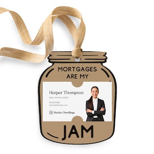May include: A brown paper jar-shaped real estate agent business card holder with the text "Mortgages Are My Jam" and a photo of a woman in a business suit. The card holder has a brown ribbon attached to the top.