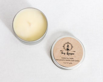 May include: A small, silver tin candle with a white soy wax candle inside. The tin has a brown label with the text "Joy League" and "Scented Soy Candles" in black text. The label also includes the text "Hand-poured in Columbia, South Carolina" and "1.5 oz/141.7 grams".