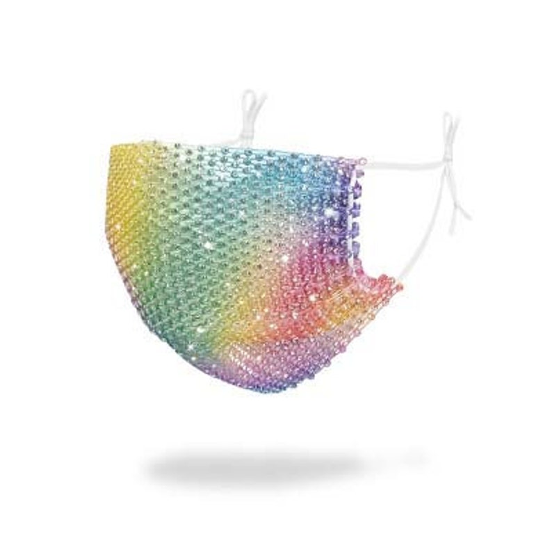 May include: A rainbow rhinestone face mask with a white elastic band. The mask is made of small, iridescent rhinestones that are sewn together in a mesh pattern.