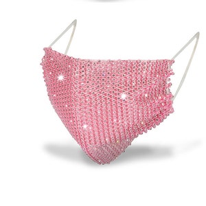 May include: Pink face mask covered in rhinestones. The mask has a clear elastic band.