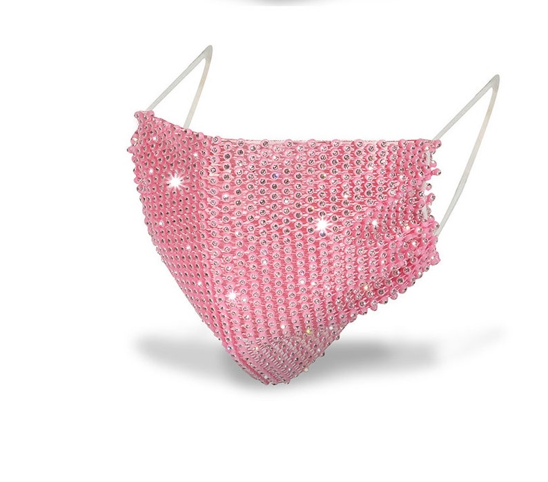 May include: Pink face mask covered in rhinestones. The mask has a clear elastic band.