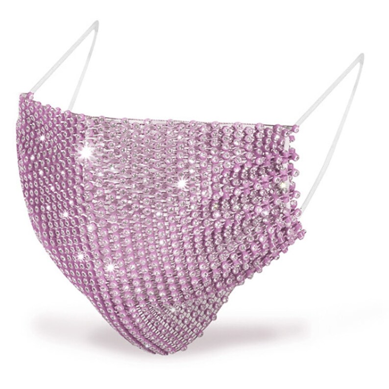 May include: A pink face mask covered in rhinestones. The mask has elastic ear loops.