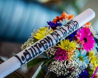 Könnte beinhalten: Ein weißer zylindrischer Schlauch mit schwarzer Beschriftung, die "Lauren De 08.13.2015" lautet, liegt auf einem Strauß bunter Blumen.