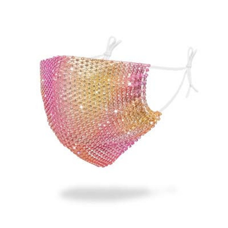 May include: A face mask made of a sparkly, iridescent mesh fabric with a gradient of pink, yellow, and gold. The mask is attached to white elastic straps.