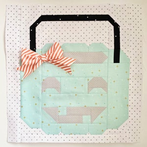 May include: A teal and grey patchwork pumpkin with a black handle and a coral and white bow. The pumpkin is on a white background with a black and white polka dot pattern.