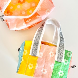 May include: Two colourful zippered pouches with a geometric floral pattern. The smaller pouch is open and the larger pouch has a silver glitter handle.