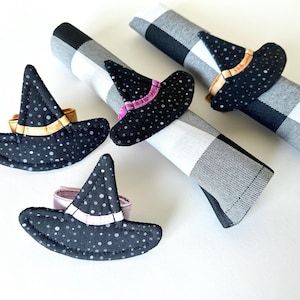 May include: A collection of Halloween-themed napkin rings shaped like witch hats. The hats are black with white polka dots and feature gold, pink, or orange bands. The napkins are black and white checkered.