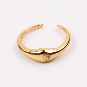 Puede incluir: Un anillo dorado con una banda lisa y redondeada y un diseño circular en el centro.