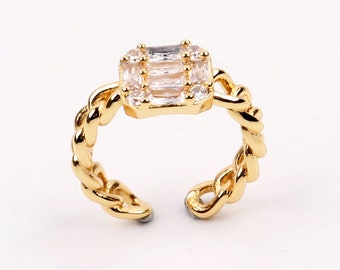 May include: A gold ring with a square-shaped clear crystal centerpiece. The ring band is a twisted chain design.