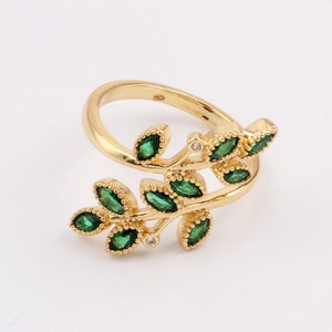 Könnte beinhalten: Ein goldener Ring mit einem filigranen Design aus grünen Blättern und kleinen weißen Steinen. Der Ring ist offen und verstellbar.