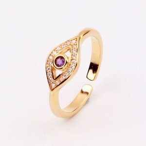 Könnte beinhalten: Goldfarbener verstellbarer Ring mit einem bösen Auge aus violettem und klarem Kristall.