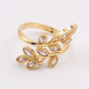 Könnte beinhalten: Ein goldener Ring mit einem zarten Design aus Blättern und klaren Kristallen. Der Ring ist offen und verstellbar.